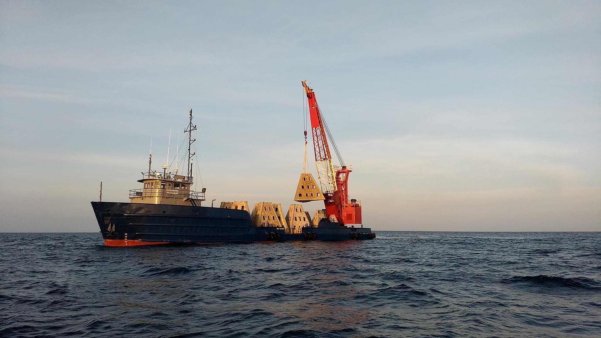Marine construction vessel operating a crane at sea near sunset