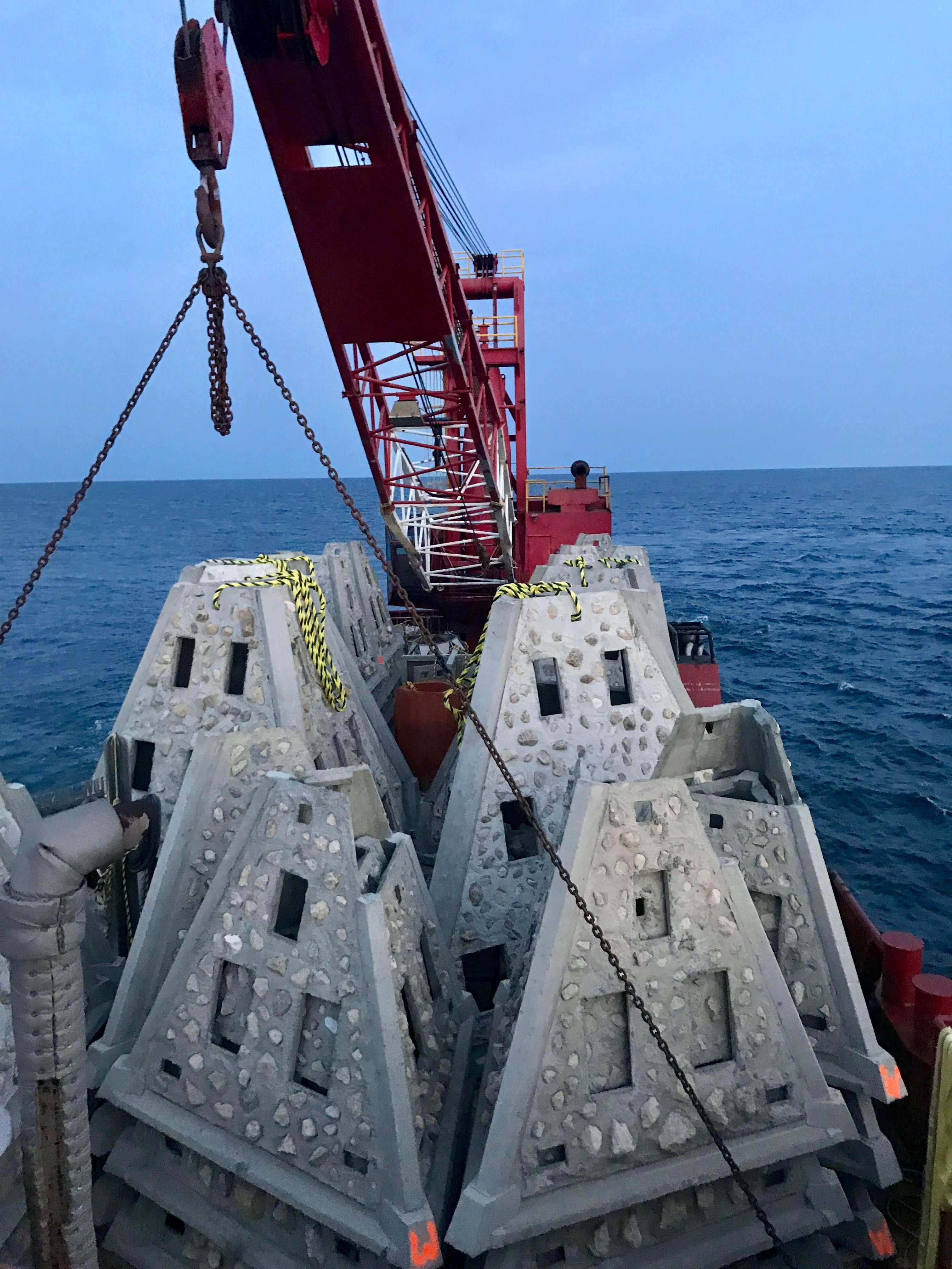 Two pyramid-shaped concrete reef modules suspended over the water during deployment