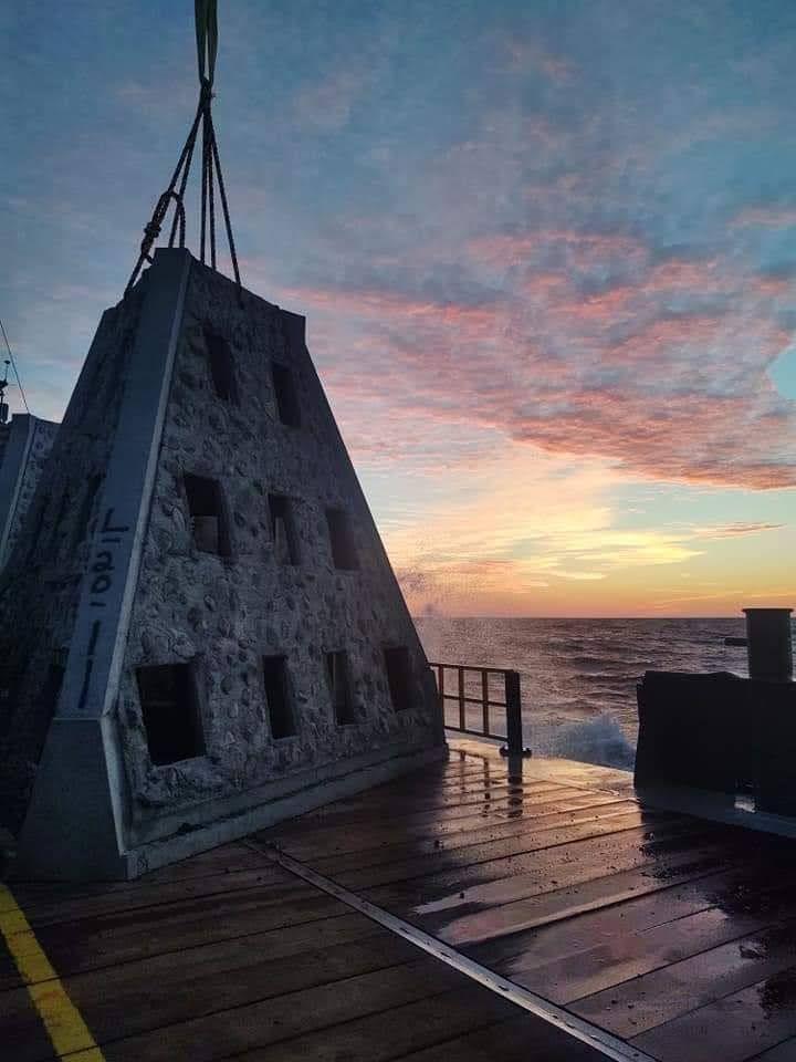 Pyramid reef module suspended from a vessel crane at sunset